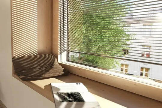 A window with closed blinds and a book resting on the sill.